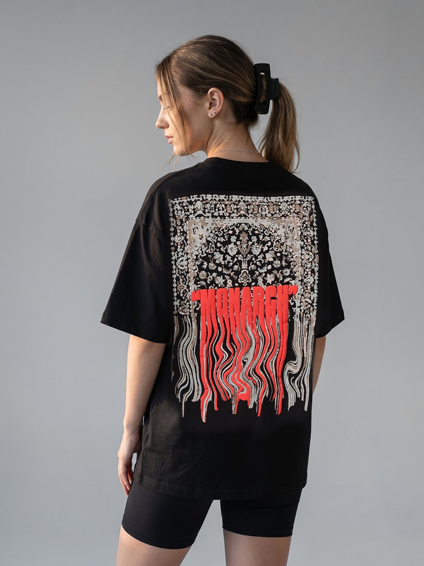 Person wearing a black t-shirt with a "MONARCH" design on the back against a gray background