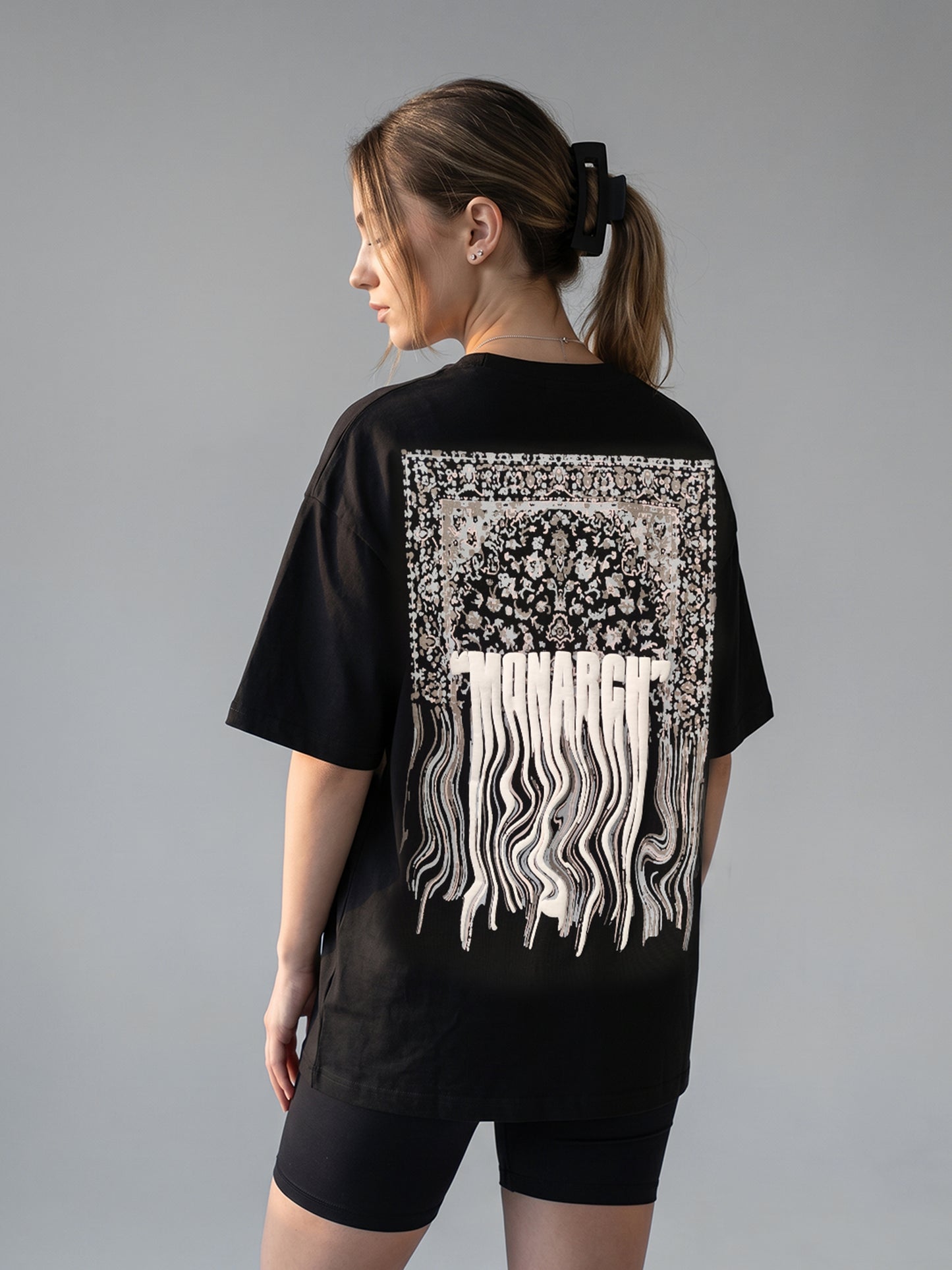 Person wearing a black t-shirt with white graphic "MPNARCH" design on the back against a gray background