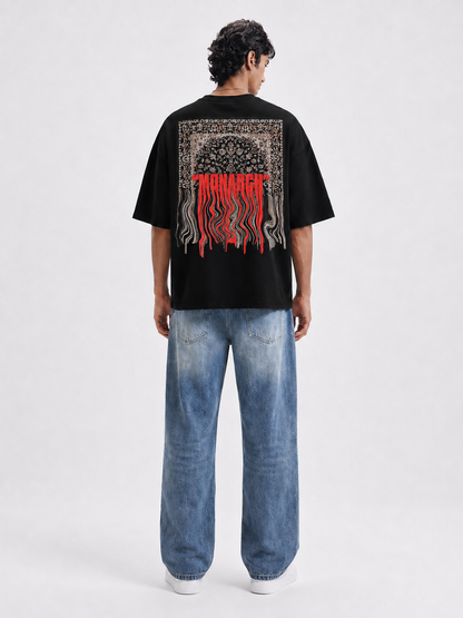 A man viewed from behind wearing a black graphic t-shirt with text "MONARCH" written on the back, paired with wide-leg blue jeans and white sneakers, against a light gray studio background.