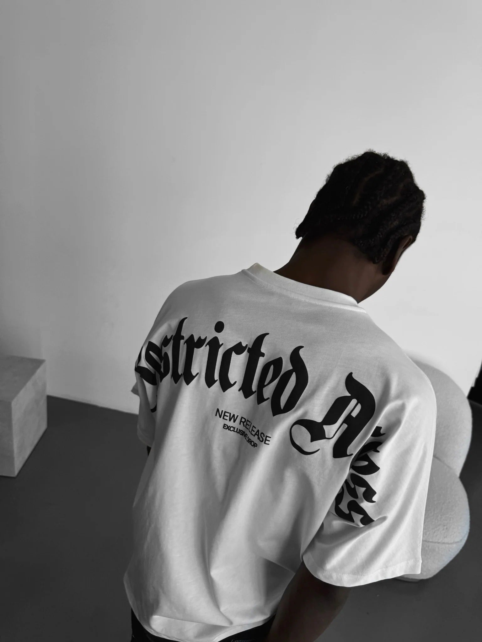 Person wearing a white tshirt with "Restricted Access" design on the back, standing indoor.
