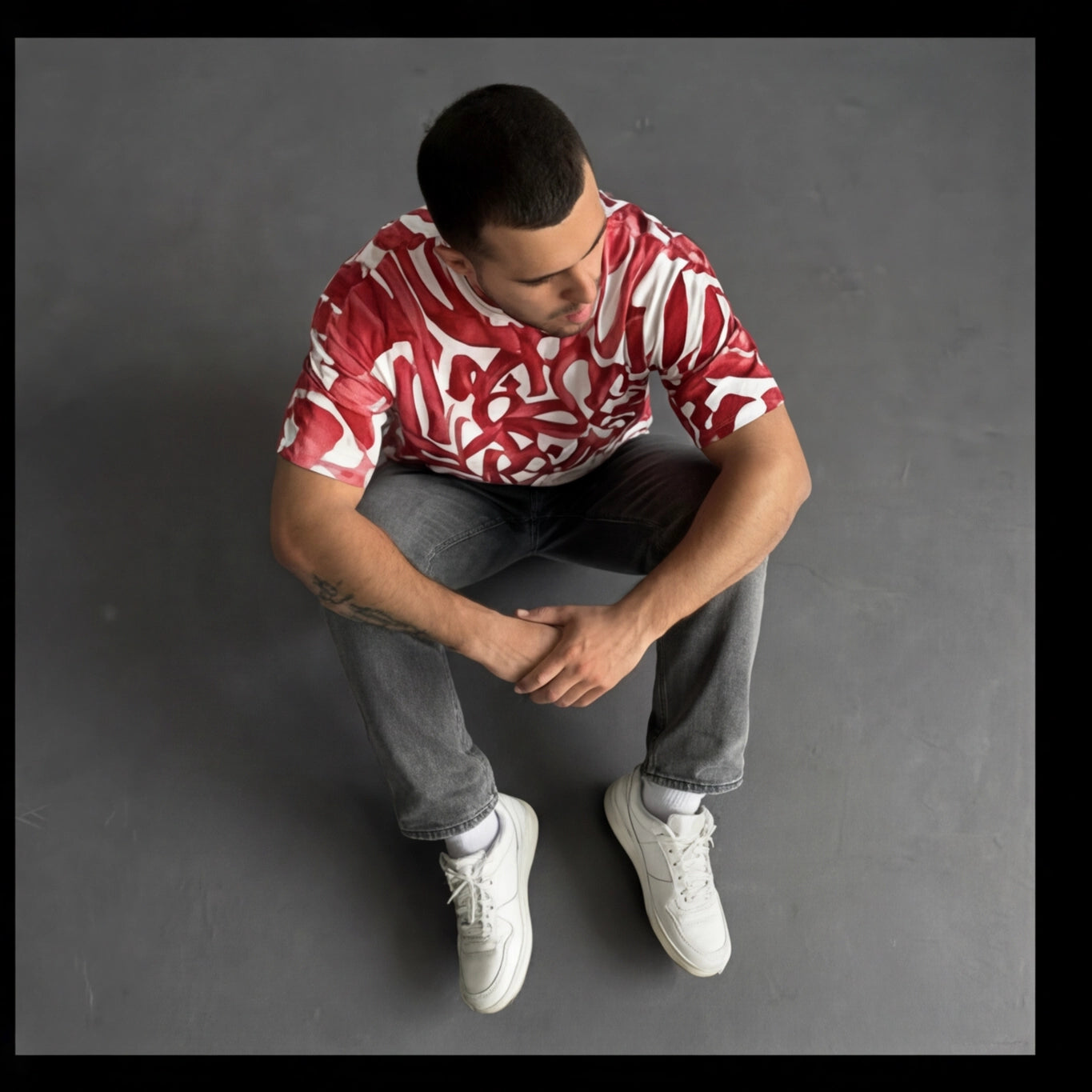 Man wearing a red and white patterned shirt sitting on a gray background