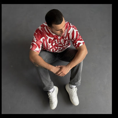 Man wearing a red and white patterned shirt sitting on a gray background