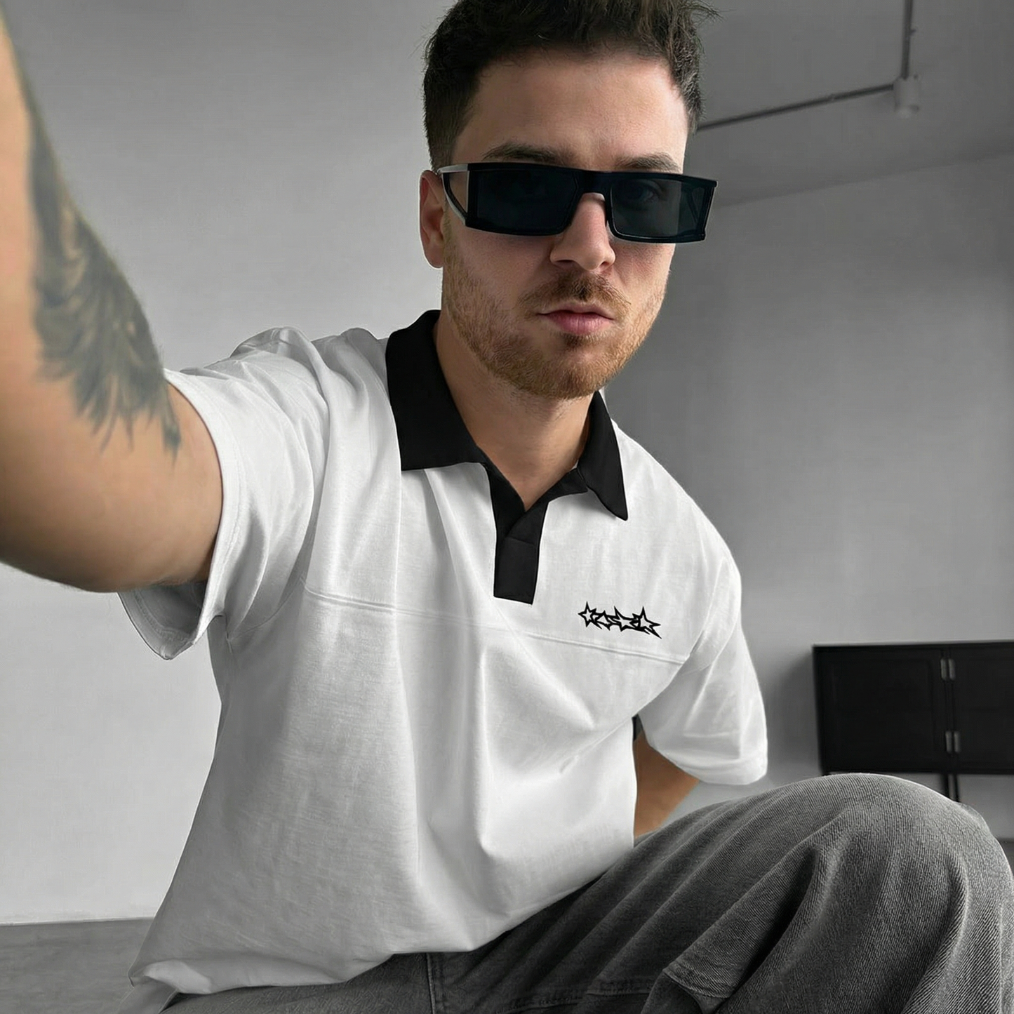 Man wearing a white polo t-shirt with a logo, sitting indoors.