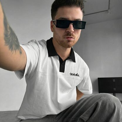 Man wearing a white polo t-shirt with a logo, sitting indoors.