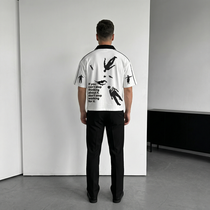 Person wearing a white Polo t-shirt with black graphics and text, standing in a minimalistic room.