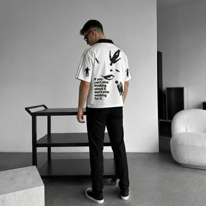 Person wearing a white Polo t-shirt with black graphics and text in a minimalistic room.