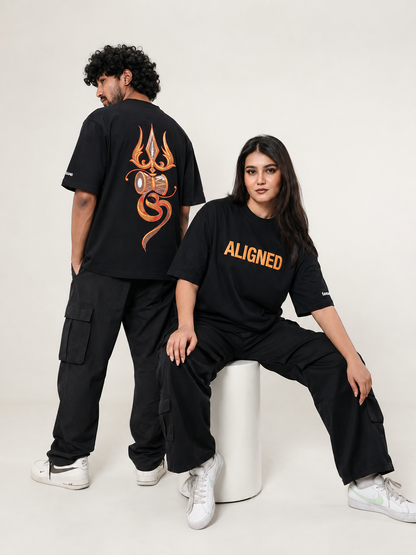 Two models wearing black oversized graphic t-shirts and black cargo pants. The model on the left stands with her back to the camera, showing a large orange and yellow graphic on the back.