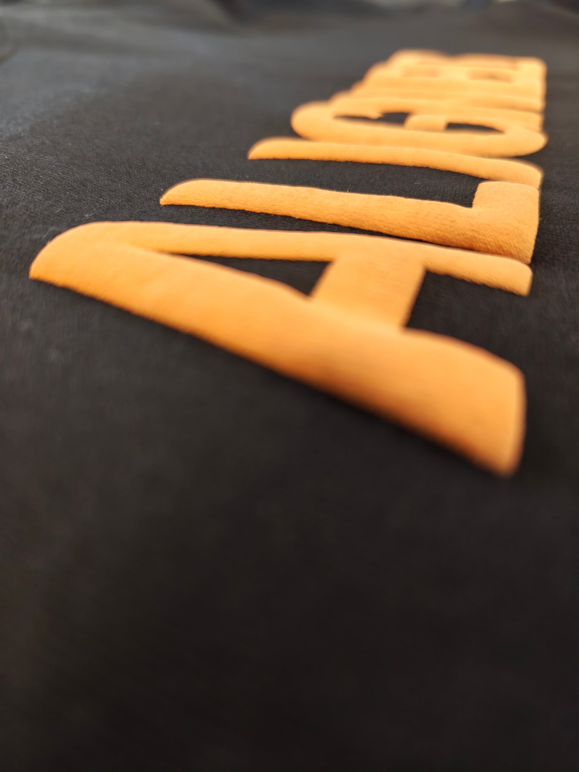 A close-up shot of a black fabric surface featuring large, raised orange letters spelling out 'ALIGN' diagonally.