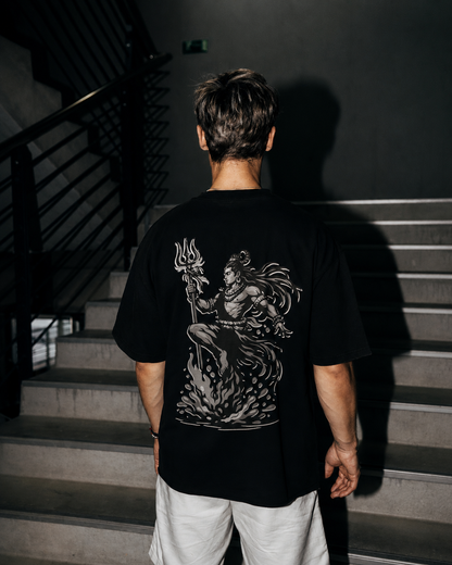 A man viewed from behind wearing a black t-shirt with a large white graphic of on the back, standing on concrete stairs in a dark indoor setting.