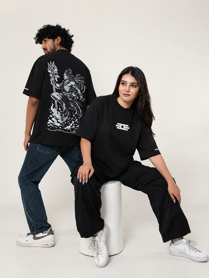 Two models in black streetwear outfits posing in front of a plain off-white studio background. The model on the left stands with his back to the camera wearing a black t-shirt with a large white graphic print on the back, paired with blue jeans and white sneakers.